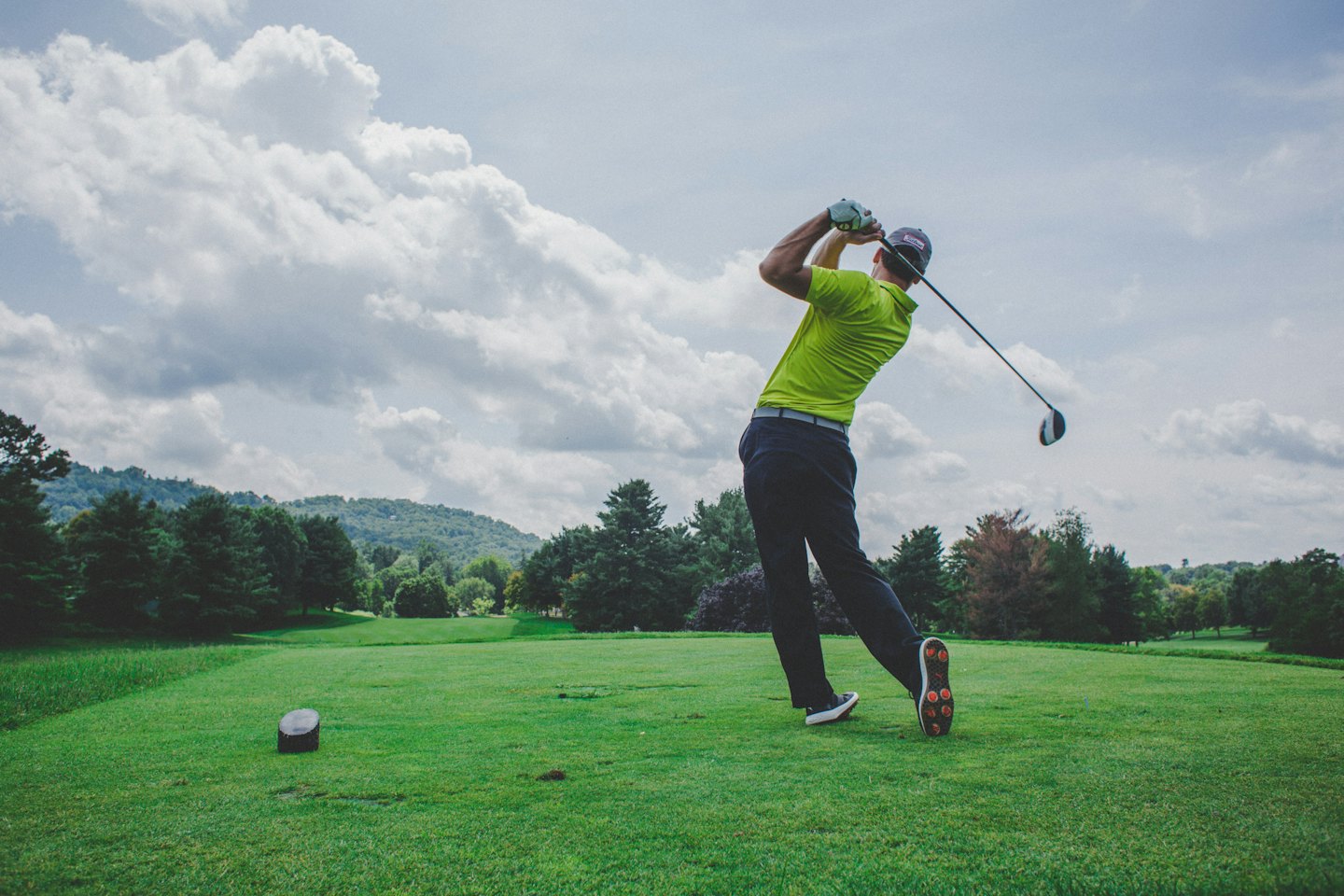 Golfer in green shirt mid-swing on a sunny course.