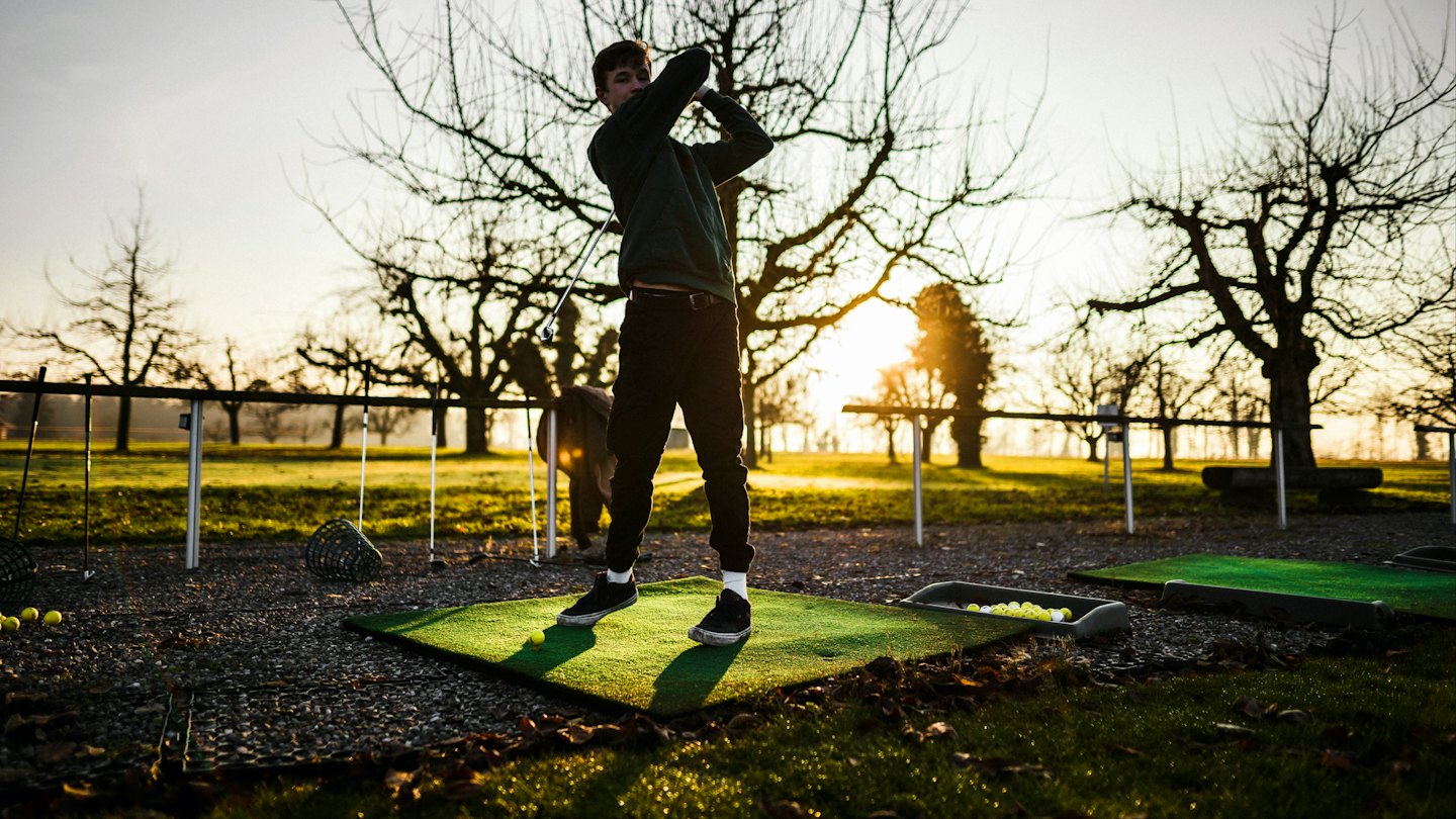 Golfer practices his swing on a driving range mat.